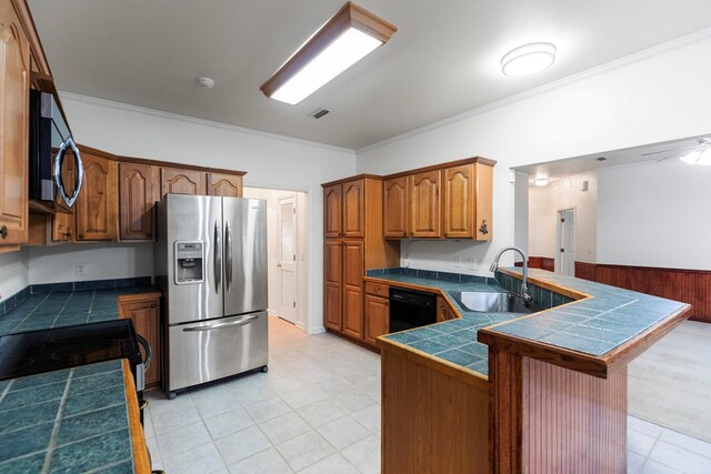 kitchen with wood walls, sink, crown molding, tile counters, and stainless steel appliances