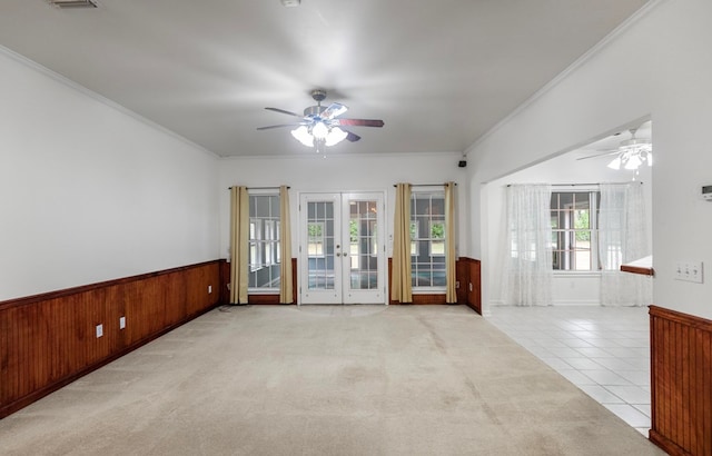 spare room with french doors, ceiling fan, crown molding, wood walls, and light tile patterned flooring