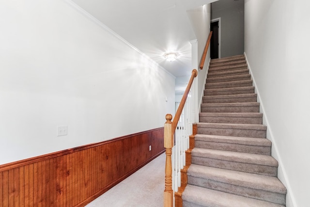 staircase featuring carpet flooring, wooden walls, and ornamental molding