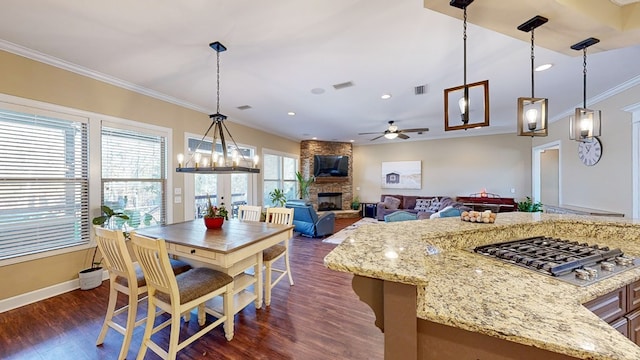 dining space with crown molding, a stone fireplace, dark wood-type flooring, and ceiling fan