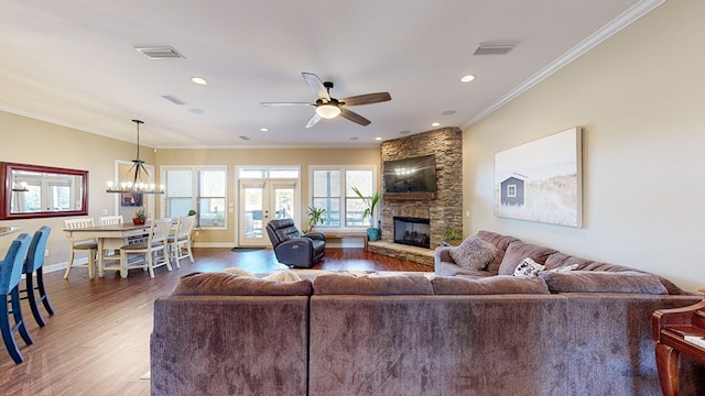 living room featuring dark hardwood / wood-style flooring, crown molding, a stone fireplace, and ceiling fan with notable chandelier