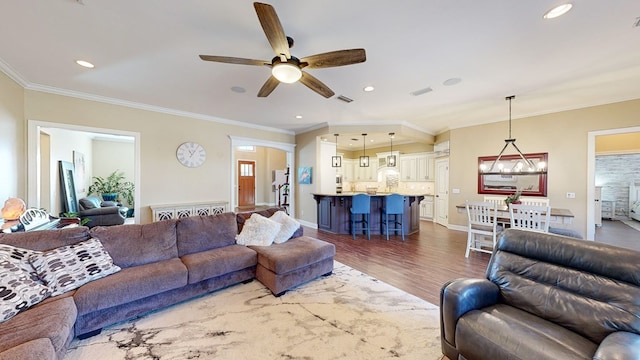 living room with ornamental molding, wood-type flooring, and ceiling fan with notable chandelier