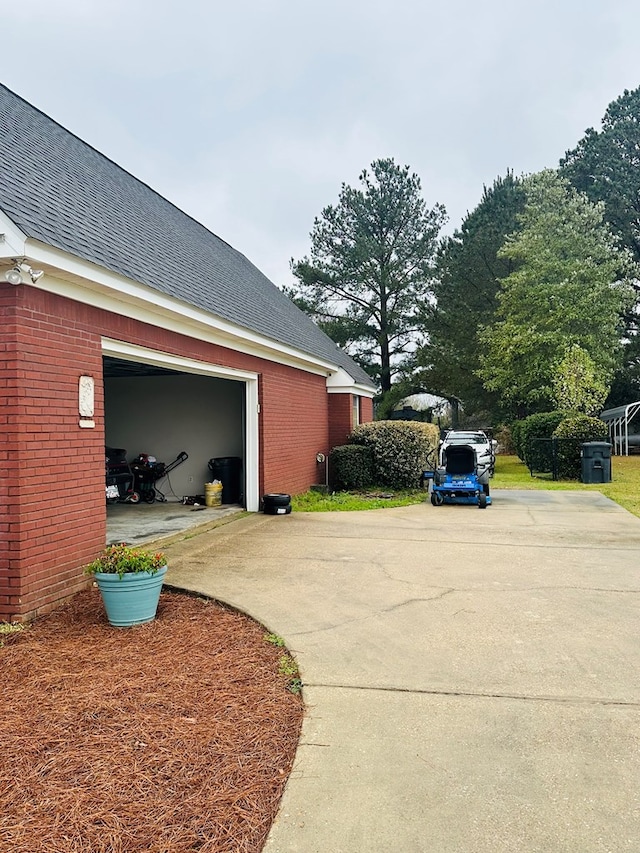 view of side of home with a garage, brick siding, driveway, and a shingled roof