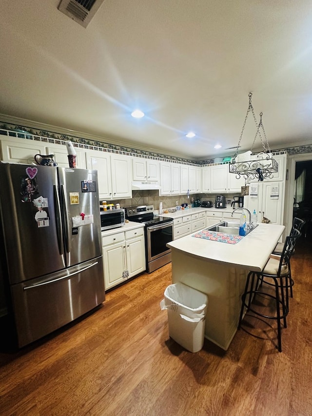 kitchen featuring white cabinetry, dark wood-style flooring, under cabinet range hood, appliances with stainless steel finishes, and a kitchen bar