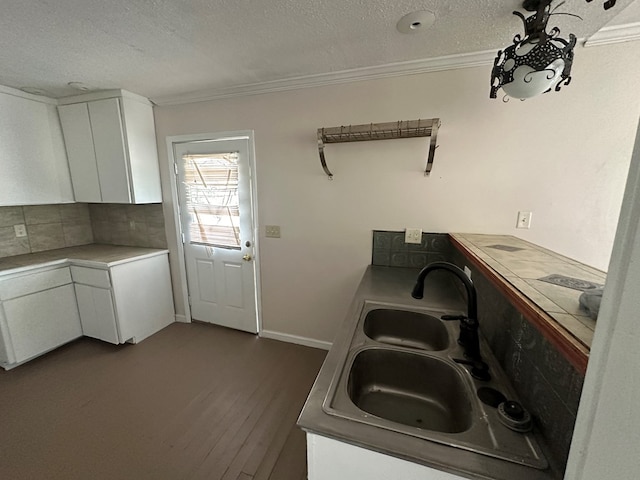 kitchen featuring a sink, backsplash, ornamental molding, and white cabinets