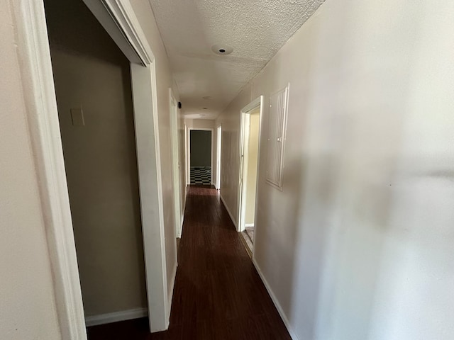 corridor with dark wood-style floors, baseboards, and a textured ceiling