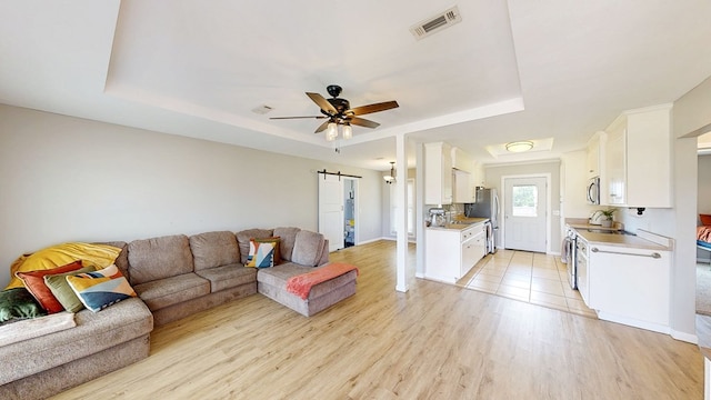 living room with visible vents, baseboards, a raised ceiling, a ceiling fan, and light wood finished floors