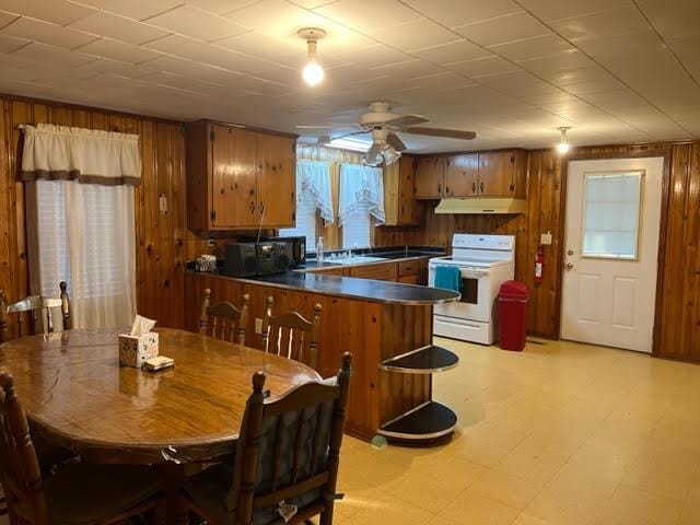 kitchen with ceiling fan, white range, kitchen peninsula, and wooden walls