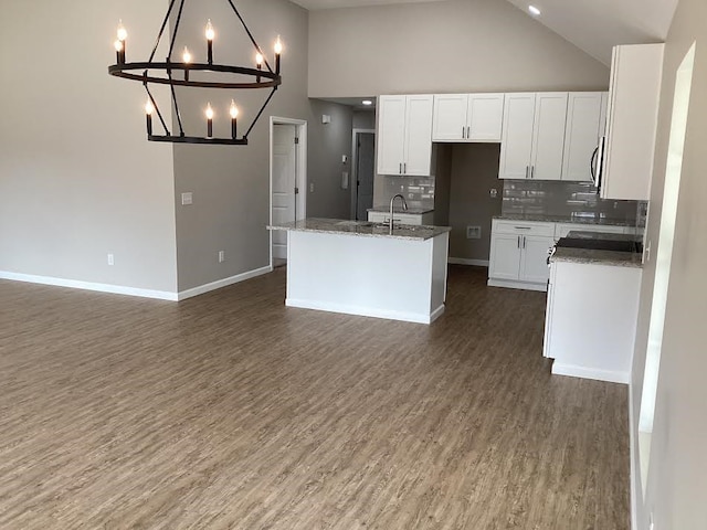 kitchen with dark stone countertops, high vaulted ceiling, an island with sink, white cabinets, and decorative backsplash