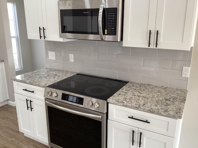 kitchen with white cabinets, appliances with stainless steel finishes, light stone countertops, and backsplash