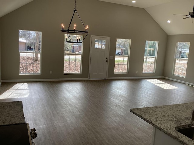 unfurnished dining area featuring ceiling fan with notable chandelier, high vaulted ceiling, and hardwood / wood-style floors