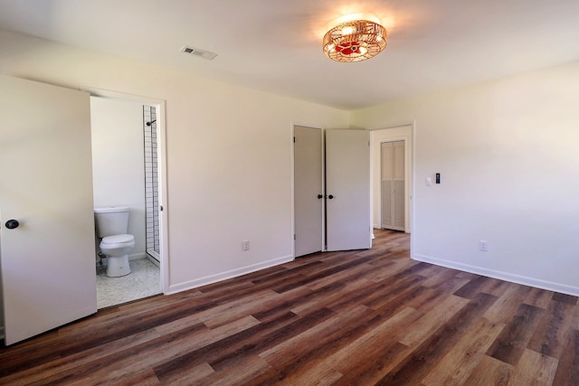 unfurnished bedroom featuring visible vents, baseboards, wood finished floors, and ensuite bathroom