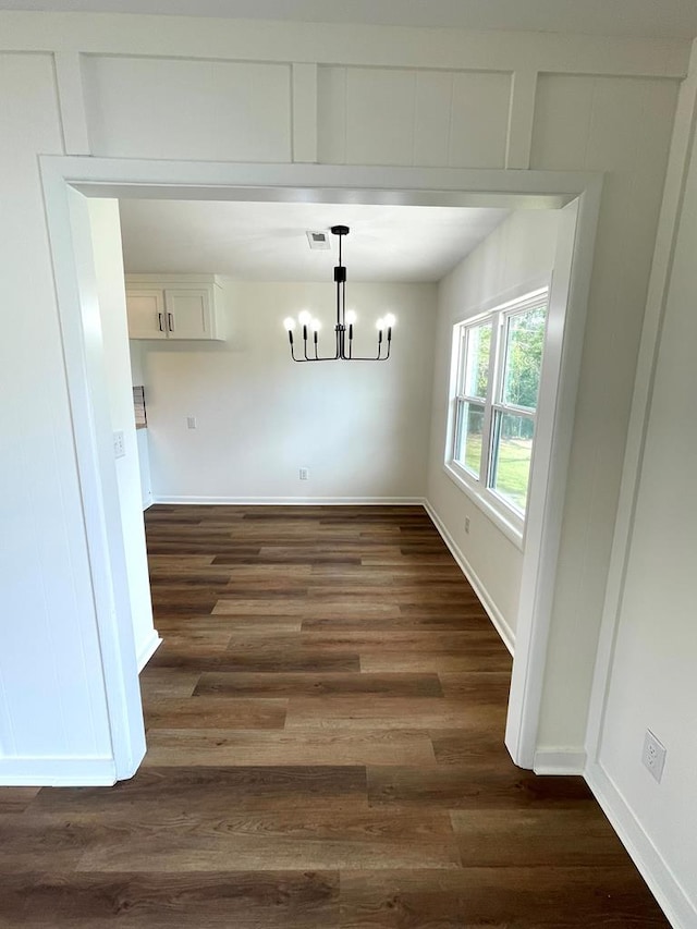 unfurnished dining area with baseboards, visible vents, a chandelier, and dark wood-type flooring