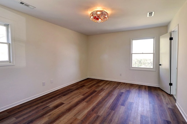 spare room with dark wood-type flooring, visible vents, and baseboards