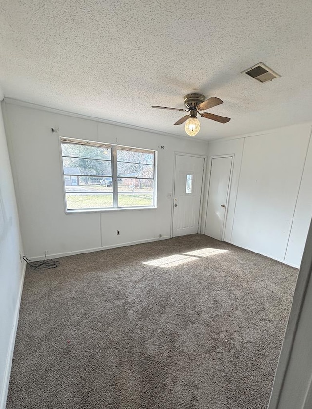 empty room featuring ceiling fan, a textured ceiling, and dark colored carpet