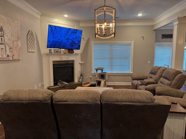 living room featuring a chandelier, ornamental molding, a fireplace with raised hearth, baseboards, and recessed lighting