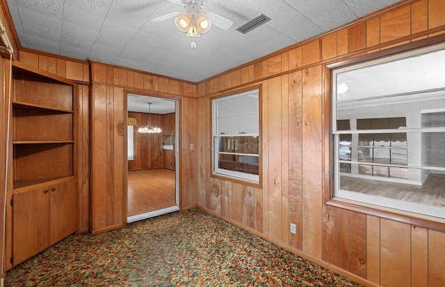 unfurnished room with light carpet, ceiling fan with notable chandelier, and wood walls