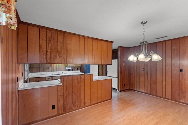 kitchen featuring pendant lighting, wooden walls, white fridge, and a notable chandelier