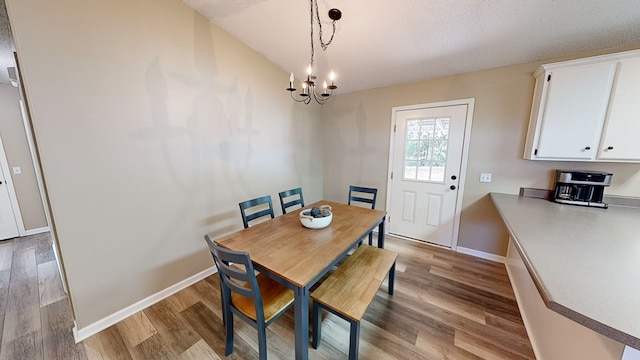 dining space with a textured ceiling, light hardwood / wood-style floors, and an inviting chandelier