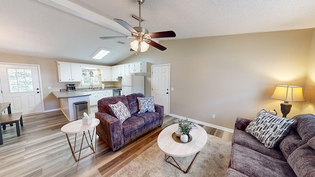 living room featuring lofted ceiling with skylight, sink, ceiling fan, and light wood-type flooring