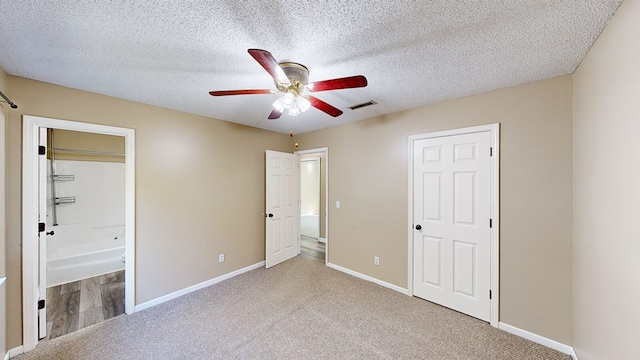 unfurnished bedroom with ceiling fan, light colored carpet, ensuite bathroom, and a textured ceiling