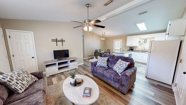 living room with sink, ceiling fan with notable chandelier, vaulted ceiling, and light wood-type flooring