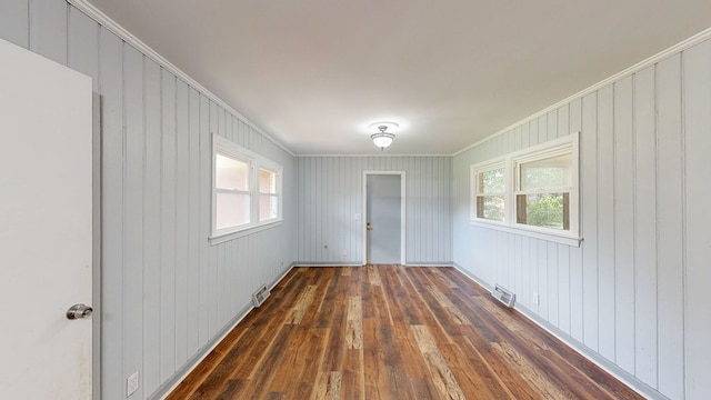 unfurnished room featuring a healthy amount of sunlight, crown molding, and dark wood-type flooring