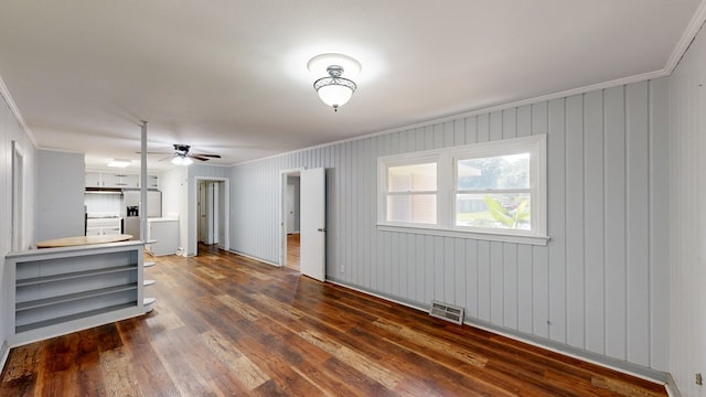 unfurnished living room featuring ornamental molding, ceiling fan, dark wood-type flooring, and wood walls