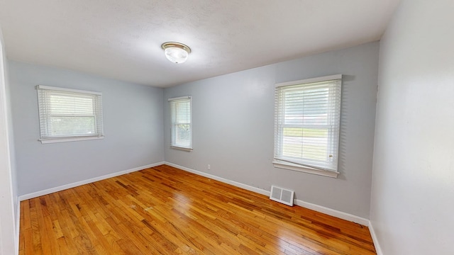 spare room with a textured ceiling, light wood-type flooring, and a healthy amount of sunlight