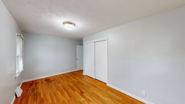 unfurnished bedroom with a textured ceiling, light wood-type flooring, and a closet