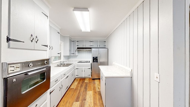 kitchen with wood walls, black appliances, sink, light hardwood / wood-style flooring, and ornamental molding