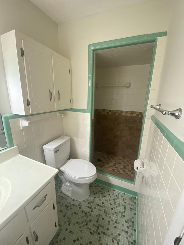 bathroom featuring vanity, tile patterned flooring, toilet, tiled shower, and tile walls