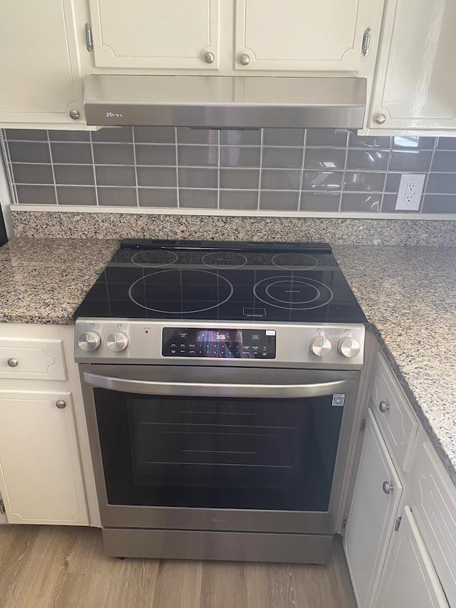 details featuring decorative backsplash, high end stove, white cabinetry, and light hardwood / wood-style flooring