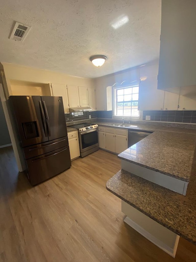 kitchen with light wood-type flooring, a textured ceiling, stainless steel appliances, sink, and white cabinetry