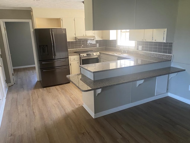 kitchen featuring sink, stainless steel appliances, kitchen peninsula, hardwood / wood-style floors, and white cabinets