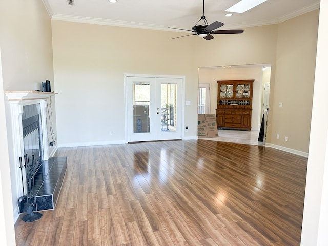 unfurnished living room featuring crown molding, baseboards, a tile fireplace, french doors, and wood finished floors