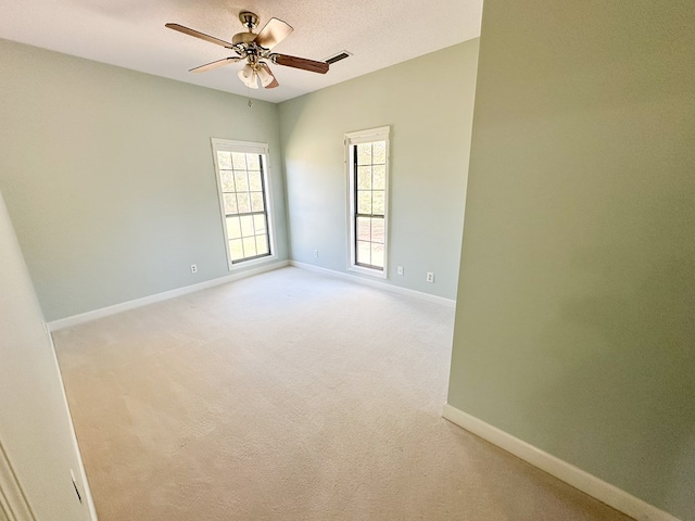 unfurnished room featuring visible vents, light colored carpet, baseboards, and ceiling fan