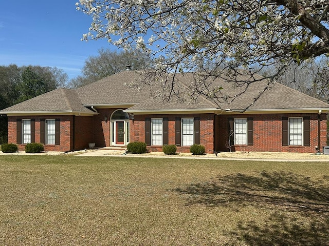 ranch-style home with a front yard, brick siding, and roof with shingles