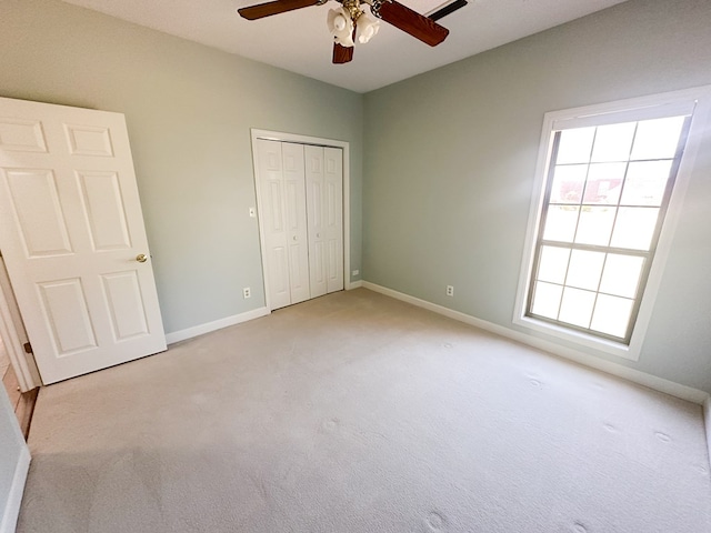 unfurnished bedroom featuring light carpet, a closet, baseboards, and a ceiling fan