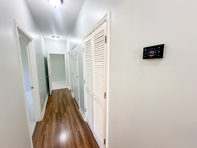 hall featuring a textured ceiling, baseboards, and dark wood-style flooring