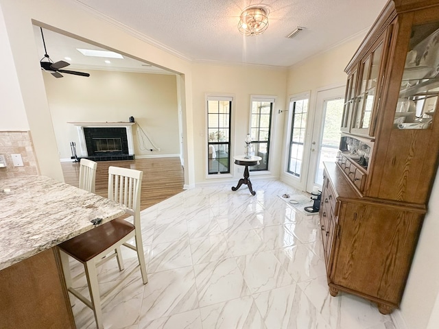 interior space with visible vents, ornamental molding, a textured ceiling, a glass covered fireplace, and marble finish floor