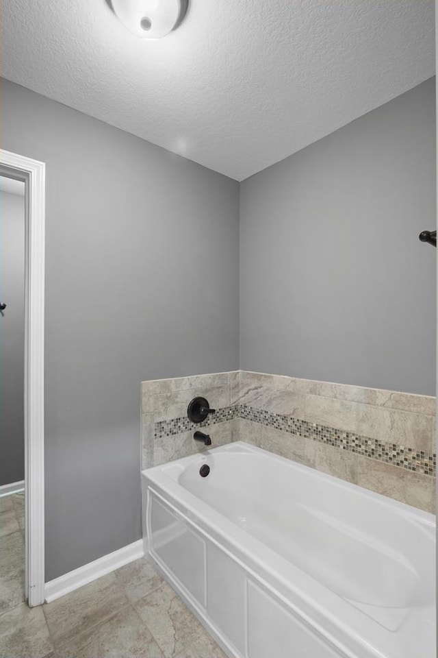 full bathroom with a textured ceiling, a bath, and baseboards