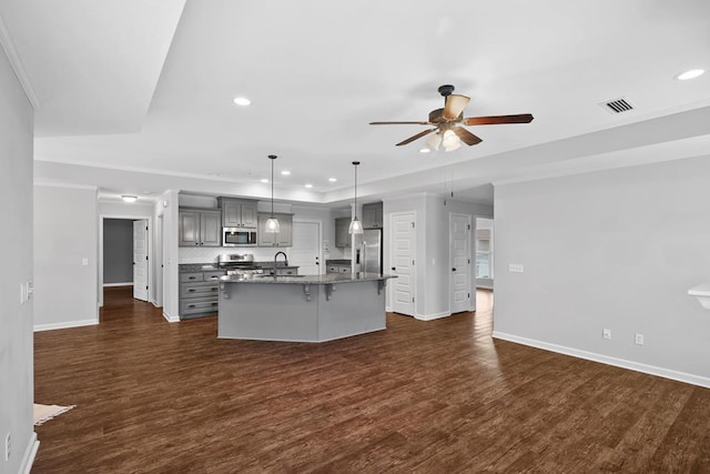 kitchen with an island with sink, dark countertops, appliances with stainless steel finishes, gray cabinetry, and pendant lighting