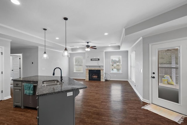 kitchen featuring decorative light fixtures, stainless steel dishwasher, a sink, an island with sink, and dark stone counters