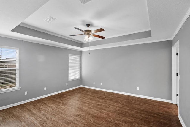 empty room with crown molding, a raised ceiling, dark wood finished floors, and baseboards