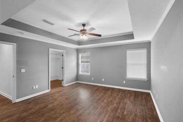 unfurnished bedroom featuring a tray ceiling, dark wood-type flooring, a walk in closet, and baseboards