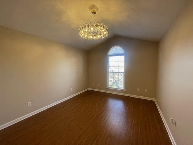 unfurnished room with lofted ceiling, an inviting chandelier, and dark hardwood / wood-style flooring