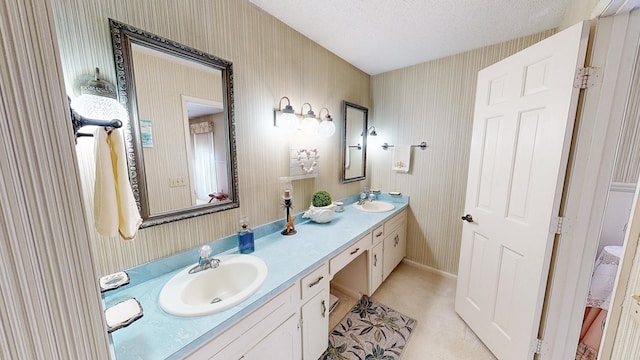 full bathroom with wallpapered walls, double vanity, and baseboards