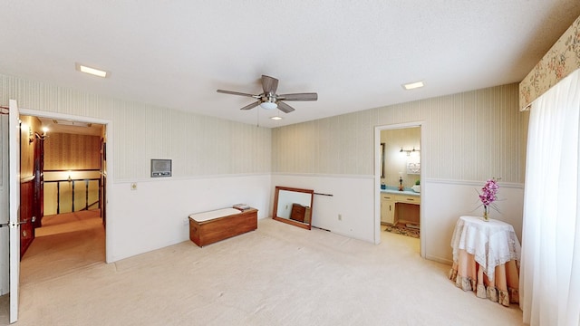 carpeted bedroom featuring wallpapered walls, a wainscoted wall, ensuite bath, attic access, and a ceiling fan