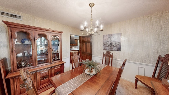 dining area featuring a chandelier, a wainscoted wall, wallpapered walls, and light carpet